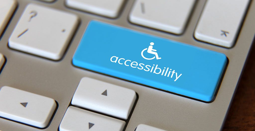 Foto de um teclado de computador. Em destaque, no meio, uma tecla azul com um ícone de cadeirante e a palavra "accessibility".